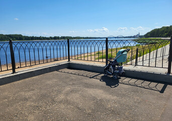 An empty children's summer stroller on the embankment near the railing overlooking the blue river...