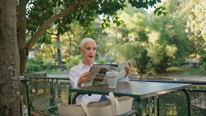 Older woman resting terrace with newspaper. Peaceful stylish lady enjoy morning