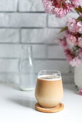 Coffee with milk in a transparent glass without an ear in the sun's rays, a bouquet with Japanese cherry blossoms stands on the back