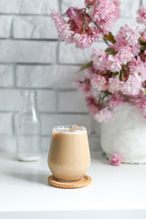 Coffee with milk in a transparent glass without an ear in the sun's rays, a bouquet with Japanese cherry blossoms stands on the back