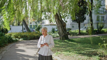 Elegant senior typing message in summer park. Grey hair lady using mobile phone