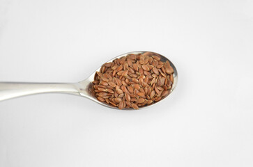 Flax seeds (linseeds) in a metal spoon on a white background, closeup, side view