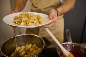 Male chef plating up Italian pasta before serving for customers. Close-up. Food and drink consumerism. Culinary. Epicure