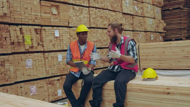 Warehouse personnel engaged in a team discussion using a digital tablet among stacks of timber.