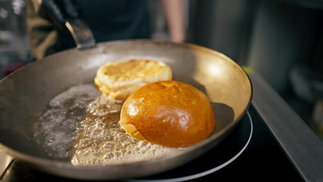 close-up in a professional kitchen of a chef's hands frying a burger bun on hot frying pan with butter