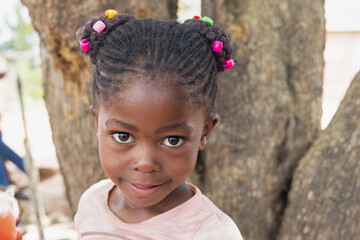 african girl with braids and beads, in front of a tree in the township
