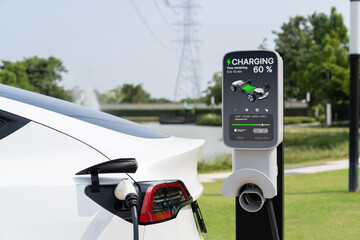Electric vehicle or EV car recharge battery at charging station connected to power grid tower...