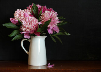 bouquet of pink peonies in a white jug on a black background. garden flowers.