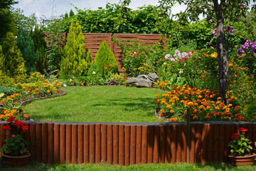 zielony trawnik w ogrodzie otoczony krzewami ozodbnymi i kolorowymi kwiatami, beautiful garden with...