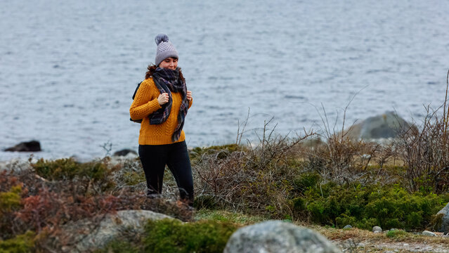 A mature woman in a yellow sweater and skarf walking by coast path, embodying the calm of a solitary coastal walk. Concept: meditation, solitude, sea exploration