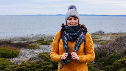 A happy mature woman in a yellow sweater smiling and looking to camera staying by chilly seaside in winter day. Copy space. Concept: cheerful spirits, winter seascape, cozy style