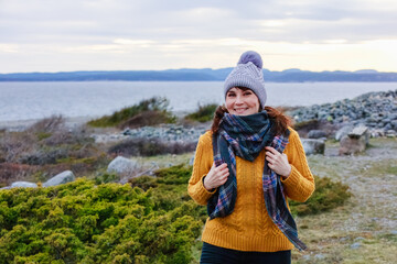 A happy mature woman in a yellow sweater looking to camera in chilly seaside in winter day.Concept: cheerful spirits, winter seascape, cozy style