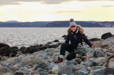 A focused woman practices the art of rock balancing on a seashore at winter dusk, creating a harmonious structure that symbolizes balance and tranquility. Concept: mindfulness, harmony, creativity