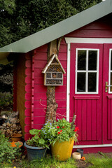 A light red small shed, gardenhouse, with some garden tools around it
