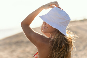 Beautiful woman in bikini posing at camera with a hat at the beach - 790400819
