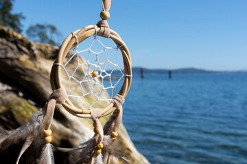 An image of a handmade dream catcher waving in soft breeze with the Pacific Ocean in the...