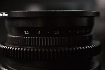 Detailed shot of aperture scale on lens, 17mm indication, focus adjustment markings for photographers, against dark, textured backdrop.