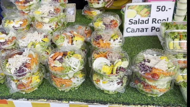 Jars of freshly made salads are lined up for sale at street food stall, showcasing mix of vibrant, healthy ingredients with clear price tag, inviting on-the-go diners to enjoy nutritious meal