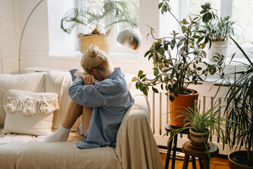 Sad lonely woman sitting on sofa at home in a full of natural light room.
