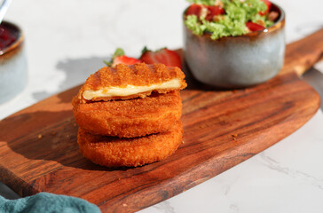 Fresh made and cutted fried camembert cheese with a side of fresh salad on wooden plate, white marble table