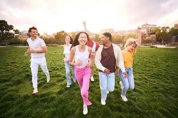 Fototapeta premium Group of young people in community celebrating and having fun outdoors at park. They laugh and run to the camera. Multiethnic group of friends together. Gathering unity in summer mood Diverse students