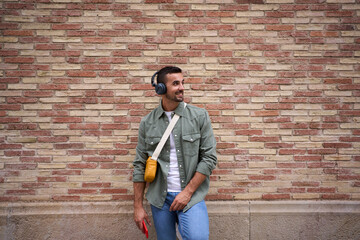Copy space of young adult Caucasian stylish man smiling with wireless headphones holding cell phone...