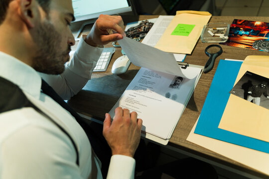 Point of view of investigator examining evidence and paperwork at his desk, part of an ongoing criminal case