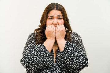 Anxious plus-size woman biting her nails in a studio with a white background