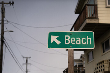 Beach sign with arrow. Beach house and power lines in background.  