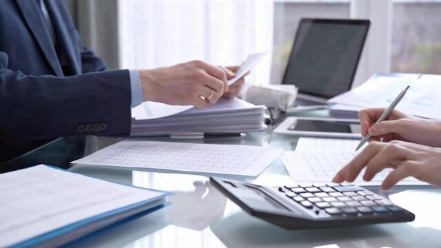 Business colleagues accountants or auditors reviewing financial data in office. Two professionals analyzing paper reports and using calculators. Audit and taxes
