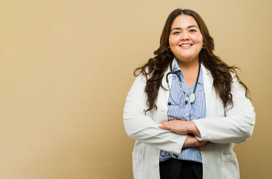Smiling plus-size female doctor with arms crossed against a beige backdrop