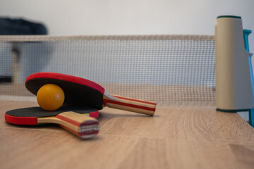 Pingpong paddles and net on indoor table at home. Portable mini pingpong set installed on a wooden table at home.b