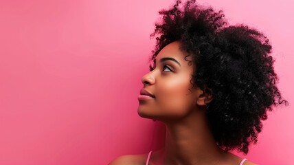 Young African woman with curly hair against pink background, looking upwards