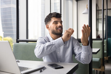 Positive young Arab businessman using invisible virtual interface, holding air, pointing at empty space, promoting innovation, modern vr technology for business, sitting at workplace