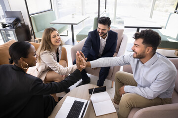 Happy successful multiethnic team achieving success, giving group high five, clapping hands at meeting in co-working office, making gesture of successful partnership, win, achievement