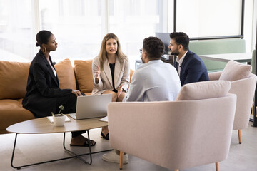 Multiethnic business team of serious coworkers discussing solutions for project, strategy decisions, talking in modern co-working space, sitting on couch, in armchair, speaking, brainstorming