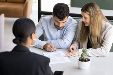 Focused married couple signing document, insurance agreement, closing real estate deal at meeting with agent, taking loan, mortgage after consulting lawyer, realtor, law advisor