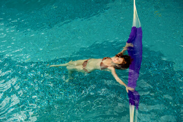 top view to young sexy bikini woman in turquoise pool spa has fun in the water with a hammock
