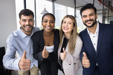 Happy successful diverse team posing for portrait in office, showing like hands, making thumb up at camera, enjoying teamwork, job success, giving positive feedback, looking at camera, smiling