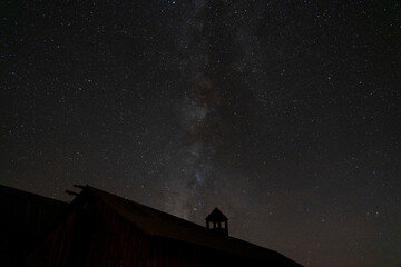 A starry night sky with the Milky Way over some farm buildings
