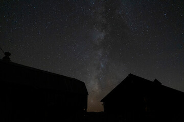 A starry night sky with the Milky Way over some farm buildings
