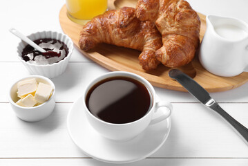 Fresh croissants, butter, jam and coffee on white wooden table. Tasty breakfast