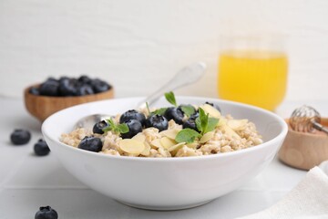 Tasty oatmeal with blueberries, mint and almond petals in bowl on white tiled table