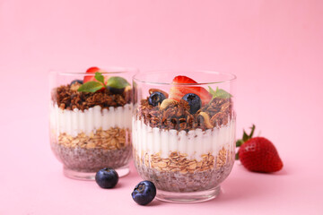 Tasty granola with berries, nuts, yogurt and chia seeds in glasses on pink background