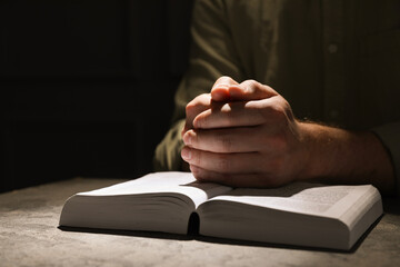 Religion. Christian man praying over Bible at table, closeup. Space for text