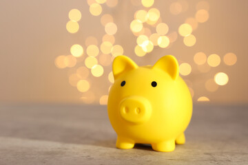 Yellow piggy bank on grey table against blurred lights, space for text