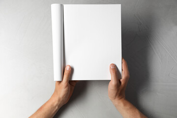 Man holding blank notebook at light grey table, top view. Mockup for design