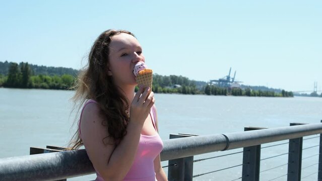 Woman licks ice cream. The girl is eating a delicious cream ice cream. Ice cream cone with strawberry flavor is her favorite summer dish. Sunset rays shine in the lens.