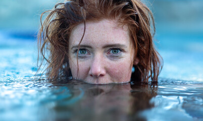 sensual dreamy portrait of sexy, young red haired woman with freckles and red wet hair, in turquoise spa pool water, head half under water