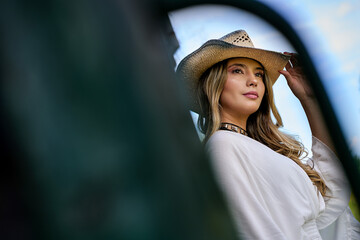 Portrait of a blonde woman wearing cowboy hat, white dress looking to sky.